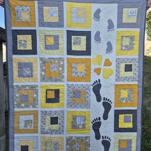 May include: Handmade quilt featuring a patchwork design with yellow, gray, and black squares. The quilt has a white center with gray footprints and yellow heart shapes. The border is gray with a small polka dot pattern.