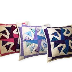 May include: Three decorative throw pillows with a white background and a colorful geometric pattern. The pillows are made of fabric and have a square shape. The patterns are made of different colored triangles and squares.