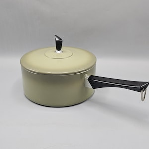 May include: A round, light beige saucepan with a matching lid. The lid features a small, black, tapered knob. The pan has a long, black, ergonomic handle extending from the side, which includes a small metal loop at the end for hanging storage.