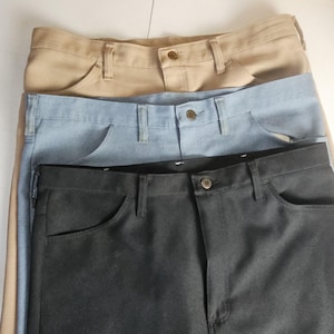 May include: Three pairs of trousers stacked vertically, featuring a tan pair at the top, a light blue pair in the middle, and a dark charcoal grey pair at the bottom. Each pair includes a waistband with belt loops, a button closure, and pockets.