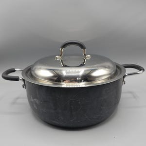 Könnte beinhalten: Ein dunkelgrauer Kochtopf mit Deckel und Griffen aus Edelstahl. Der Topf hat zwei Seitengriffe und einen Bügelgriff am Deckel. Der Deckel ist glänzend und reflektiert das Licht. Der Topf steht auf einer grauen Oberfläche.