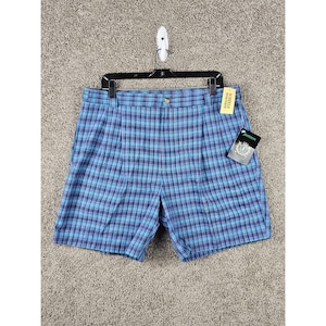 May include: Blue and purple plaid shorts with a button closure and pleats. The shorts are hanging on a black hanger with a tag that says "Scheels" and another tag that says "Jantzen".