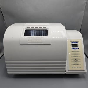 May include: A white West Bend bread maker with a digital display and control panel. The appliance has a rectangular shape with a curved top and a viewing window. The control panel includes buttons for various settings.