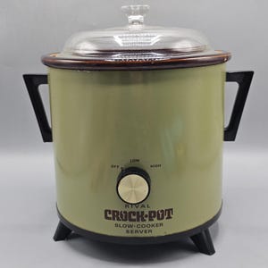Puede incluir: Una olla de cocción lenta Rival Crock-Pot de color verde oliva vintage con tapa de cristal transparente, asas laterales negras y base negra. El frente tiene un mando central con ajustes Off, Low y High y el texto Rival Crock-Pot Slow-Cooker.