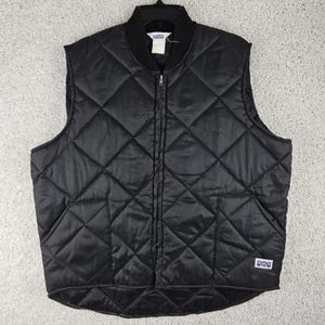 May include: Black quilted vest with a diamond pattern, a zip-up front, and two front pockets. The vest has a black ribbed collar and a small label on the lower right side. The vest is hanging on a black hanger.