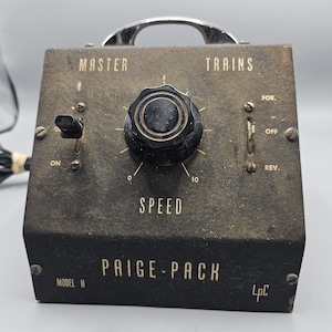 May include: Vintage Paige-Pack model train power supply. The black box features a speed control knob, on/off switch, and forward/reverse switch. The text "MASTER TRAINS SPEED" and "PAIGE-PACK" are visible.