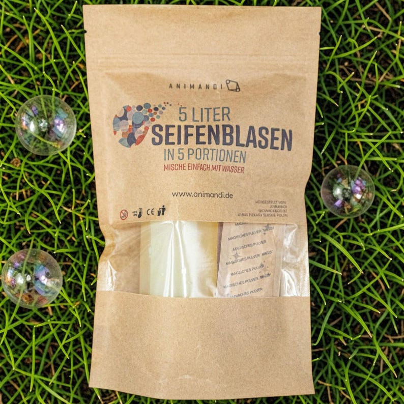 May include: A brown paper bag of bubble solution, with the text "5 Liter Seifenblasen" and "Mische einfach mit Wasser". The bag contains a clear, rectangular block and small packets. Three iridescent bubbles are scattered on the green grass.
