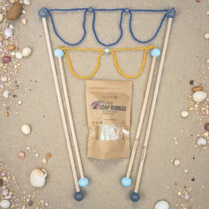 Può includere: Due bacchette per bolle di sapone con manici in legno e cappi in corda blu o gialla, accompagnate da un sacchetto di carta marrone con l'etichetta 5 LITER SOAP BUBBLES IN 5 PORTIONS. Le bacchette presentano terminali sferici azzurri e grigi.