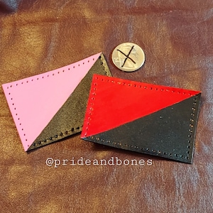 Puede incluir: Dos parches de cuero con un diseño dividido en diagonal. El parche superior es rosa y negro, el parche inferior es rojo y negro. Los parches están cosidos alrededor de los bordes.