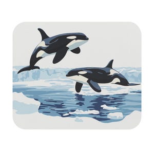 May include: A square mousepad featuring a graphic illustration of two orcas in a polar environment. The orcas are black and white, with one leaping out of the water. The background depicts ice and water in shades of blue and white.