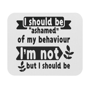 May include: A white square coaster with rounded corners. The coaster features black text that reads "I should be 'ashamed' of my behaviour I'm not but I should be". Decorative leaf accents are also included.