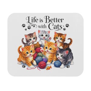 May include: A white square coaster featuring six cartoon kittens of various colors playing with yarn balls and a small fish. The text "Life is Better with Cats" is displayed in elegant script above the kittens, with paw prints scattered around the edges.