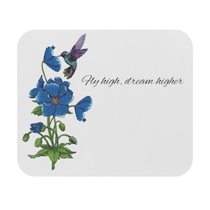 May include: White rectangular mousepad featuring a blue floral design with a hummingbird. The hummingbird is depicted with purple and green feathers. The text "Fly high, dream higher" is written in black cursive.