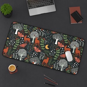 May include: A black rectangular desk mat featuring a forest design with trees, deer, butterflies, stars, and a crescent moon in orange, white, and green. The mat has a black border and is designed for a desk.