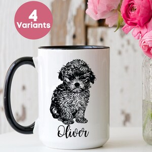 May include: White ceramic mug with a black handle and rim, featuring a black and white illustration of a puppy and the name "Oliver". A pink circle with "4 Variants" is in the upper left. Pink flowers in a glass jar are to the right.