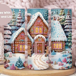 May include: A set of three 20 oz stainless steel tumblers with a winter wonderland design featuring a gingerbread house, snow-covered trees, and candy canes. The tumblers are personalized with the name "Sophia".