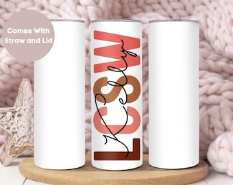 May include: Three stainless steel tumblers, one with the name "Kelsey" written in black script with pink, brown, and orange accents. The tumblers are on a wooden surface.