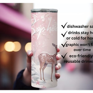 May include: A pink and white stainless steel tumbler with a deer and snowflakes design. The tumbler has the name "Sophia" written on it. It is dishwasher safe, keeps drinks hot or cold for hours, and is eco-friendly.