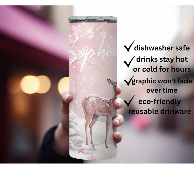 May include: A pink and white stainless steel tumbler with a deer and snowflakes design. The tumbler has the name "Sophia" written on it. It is dishwasher safe, keeps drinks hot or cold for hours, and is eco-friendly.