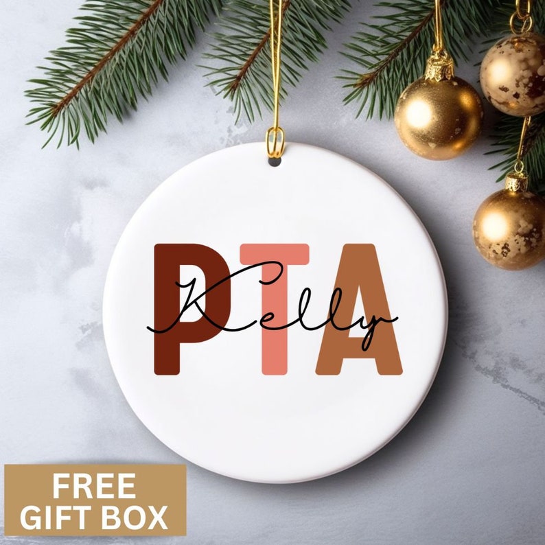 May include: White ceramic ornament with the letters PTA in brown, pink, and orange. The word "Kelly" is written in cursive below the letters.