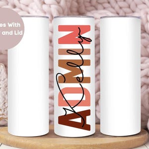 May include: Three white stainless steel tumblers with lids. The center tumbler has the word "ADMIN" written in a stylized font with brown, pink, and red colors. The text "Comes With Straw and Lid" is written in white on a pink background in the top left corner of the image.