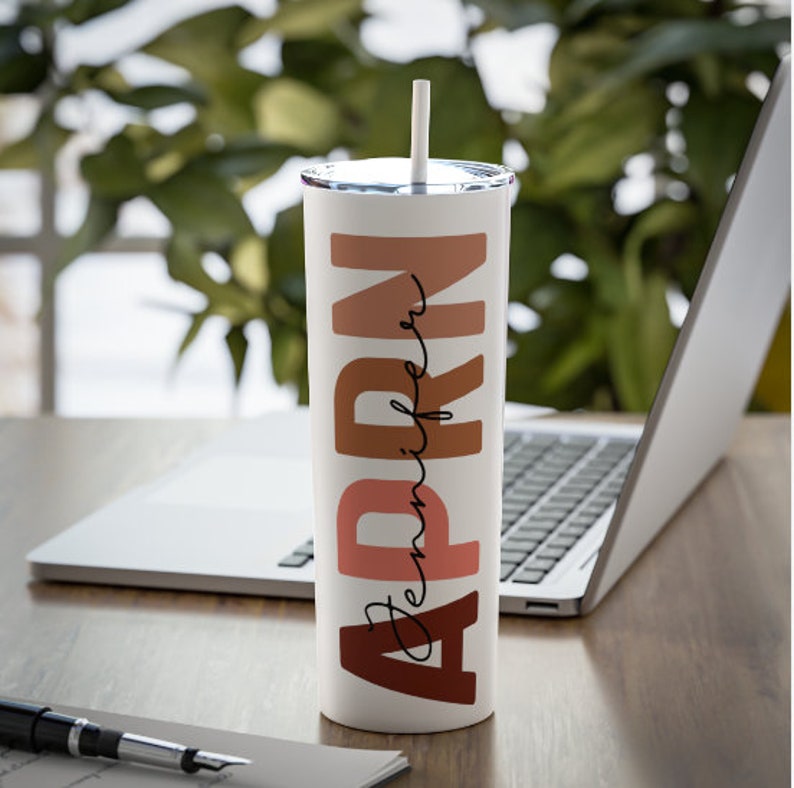 May include: A white stainless steel tumbler with a brown, pink, and orange design that says "APRN Jennifer".
