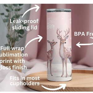 May include: A pink stainless steel tumbler with a full wrap sublimation print of two deer in a snowy forest. The tumbler has a leak-proof sliding lid and fits in most cupholders. It is BPA free.