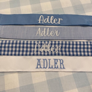 May include: Four blue and white fabric ribbons with the name "Adler" embroidered in white on each ribbon.