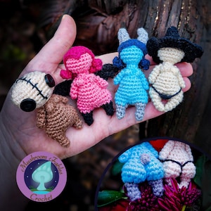 Może przedstawiać: Kolekcja ręcznie robionych szydełkowych lalek w różnych kolorach, w tym różowym, niebieskim i beżowym. Każda lalka ma unikalne cechy, takie jak kapelusze i ubrania. Lalki są trzymane w dłoni, z logo w lewym dolnym rogu.