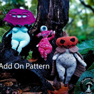 Puede incluir: Tres figuras de amigurumi de crochet: un personaje con forma de hongo con un sombrero morado, una criatura rosa de un ojo y una figura con cabeza de calabaza con una capa marrón. Las figuras están sentadas en un tocón de árbol con el texto "Add On Pattern" delante de ellas. La imagen también incluye un logotipo para "Mushroom Fables Crochet".