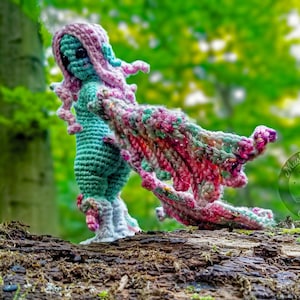 Amigurumi doll that is a gurl with wings. Winged Harpy in the forest looks like a fairy.