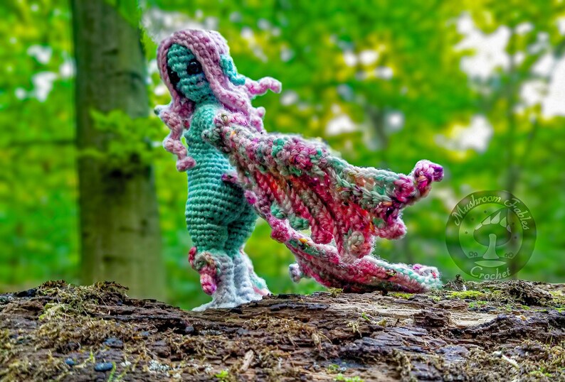 Amigurumi doll that is a gurl with wings. Winged Harpy in the forest looks like a fairy.