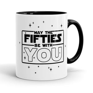 May include: White ceramic coffee mug with a black rim and handle. The mug has a black and white graphic that says "May the Fifties Be With You" with stars around the graphic.