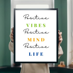 Puede incluir: Una impresión enmarcada con el texto "Positive Vibes Positive Mind Positive Life" en escritura negra. Las palabras "Vibes", "Mind" y "Life" están en diferentes colores: verde, naranja y azul.