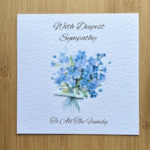 May include: A sympathy card featuring a bunch of blue forget-me-not flowers with the text "With Deepest Sympathy" and "To All The Family".