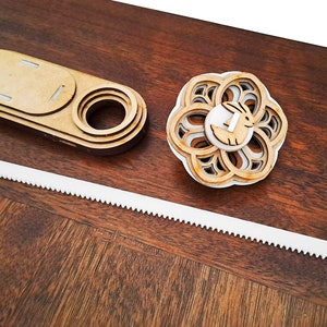 Peut inclure: Un ensemble de service à gâteau en bois avec une lame dentelée blanche, une pièce décorative en forme de fleur avec un motif de lapin et une boîte en bois avec une ouverture circulaire. Les articles sont disposés sur une surface en bois foncé.