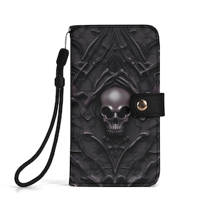 Op de afbeelding: Een zwarte portemonnee met een schedelontwerp. De portemonnee heeft een gedetailleerd reliëfpatroon en een polsbandje. De schedel is gecentreerd op de voorkant, met een zwarte band en een gouden knoopsluiting.