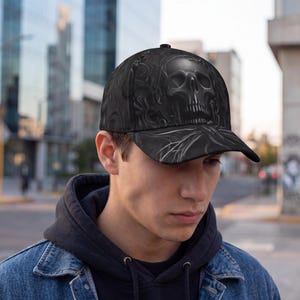 Pode incluir: Boné de beisebol preto com um design de caveira. O boné tem uma aba curva e uma coroa estruturada. O gráfico da caveira é detalhado com sombreamento e destaques, criando um efeito tridimensional. O boné é feito de tecido durável.