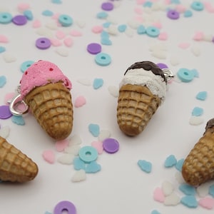 May include: Four miniature ice cream cone charms with different flavors: pink, green, white with chocolate topping, and brown. The charms are on a white background with colorful sprinkles.