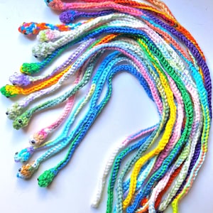 May include: A collection of colorful crocheted snake-shaped bookmarks. The bookmarks are made with a variety of bright colors, including pink, blue, green, yellow, and orange. Each bookmark has a small crocheted snake head at the top.