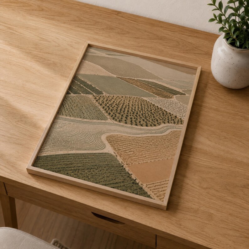 Pode incluir: Uma impress&atilde;o retangular emoldurada com uma vista a&eacute;rea de campos agr&iacute;colas em tons de verde s&aacute;lvia, oliva, bege e ocre. A obra exibe um mosaico de padr&otilde;es texturizados que representam v&aacute;rias culturas dentro de uma moldura de madeira clara.