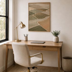 Pode incluir: Uma impress&atilde;o de arte de parede retangular emoldurada apresentando uma vista a&eacute;rea de campos agr&iacute;colas em tons de verde, bege e marrom. A obra de arte &eacute; exibida em uma parede lisa acima de uma mesa de madeira, mostrando um padr&atilde;o de paisagem texturizado.