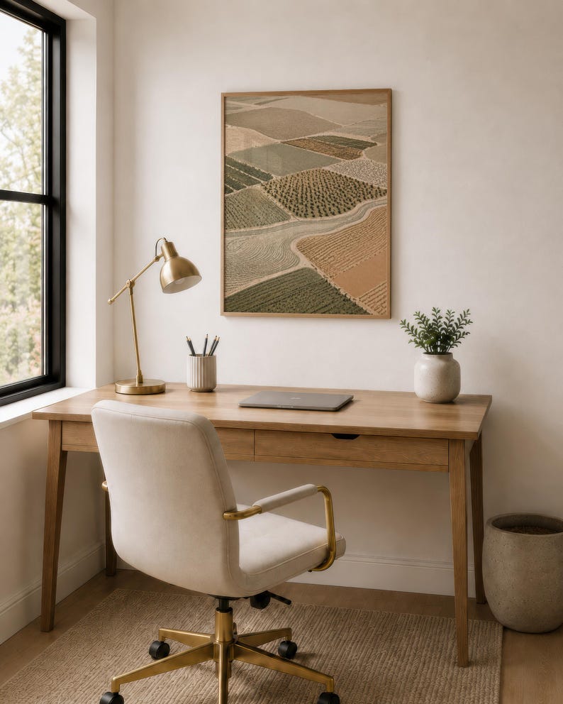 Pode incluir: Uma impress&atilde;o de arte de parede retangular emoldurada apresentando uma vista a&eacute;rea de campos agr&iacute;colas em tons de verde, bege e marrom. A obra de arte &eacute; exibida em uma parede lisa acima de uma mesa de madeira, mostrando um padr&atilde;o de paisagem texturizado.