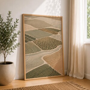 Pode incluir: Uma impress&atilde;o de arte de parede retangular emoldurada apresentando uma vista a&eacute;rea de campos agr&iacute;colas em tons de verde s&aacute;lvia, oliva, bege e castanho. A paisagem mostra v&aacute;rios padr&otilde;es de cultivo, texturas e um caminho sinuoso numa moldura de madeira clara.