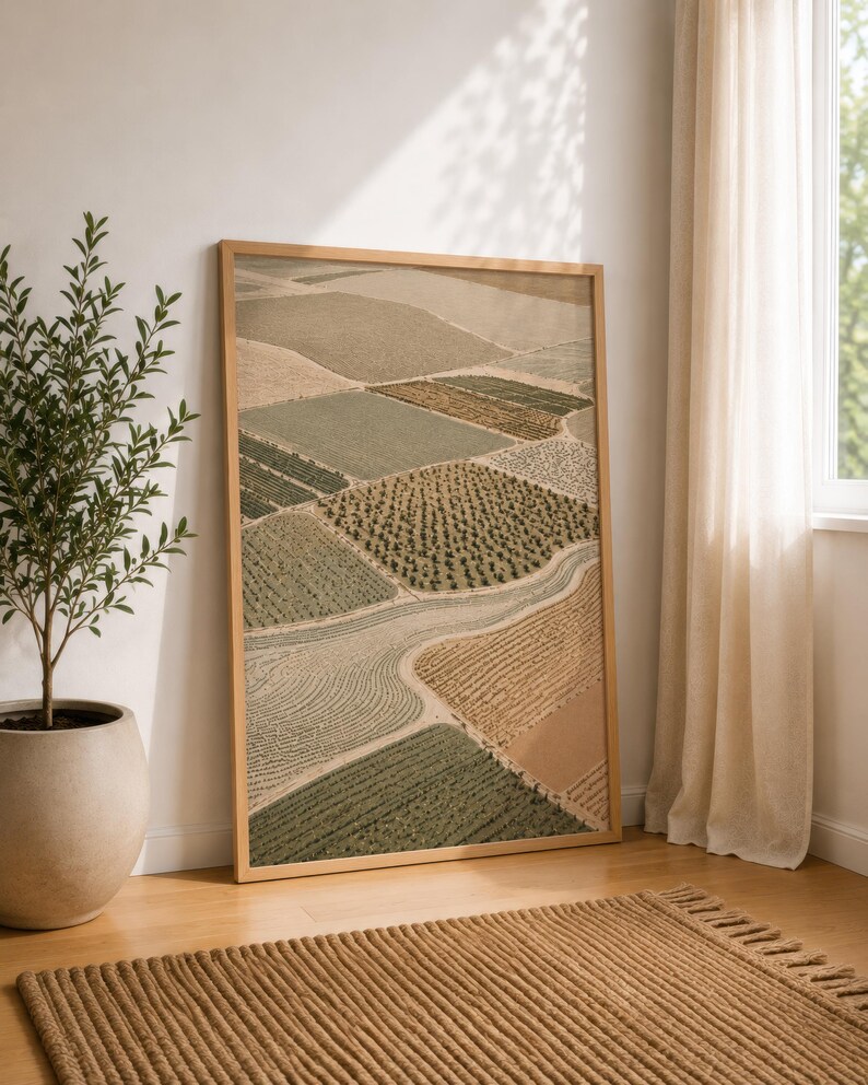 Pode incluir: Uma impress&atilde;o de arte de parede retangular emoldurada apresentando uma vista a&eacute;rea de campos agr&iacute;colas em tons de verde s&aacute;lvia, oliva, bege e castanho. A paisagem mostra v&aacute;rios padr&otilde;es de cultivo, texturas e um caminho sinuoso numa moldura de madeira clara.