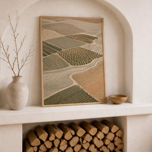 Pode incluir: Uma impress&atilde;o art&iacute;stica retangular emoldurada apresentando uma vista a&eacute;rea de campos agr&iacute;colas em tons de verde s&aacute;lvia, oliva, bege e ocre, separados por caminhos sinuosos. A obra &eacute; exibida em uma moldura fina de madeira clara.