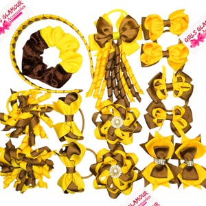 Può includere: Una collezione di accessori per capelli gialli e marroni che include un cerchietto intrecciato, un elastico in velluto, vari fiocchi in nastro, nastri a spirale e due clip a forma di fiore con perle e strass al centro.