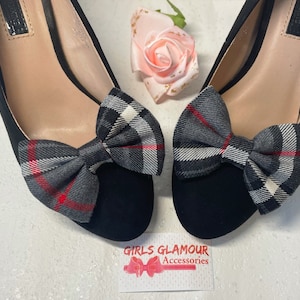 Op de afbeelding: Een paar zwarte schoenen met een geruite strik op elke schoen. De schoenen staan op een wit oppervlak. De tekst "Girls Glamour Accessories" is zichtbaar op een kaart in de rechterbenedenhoek van de afbeelding.