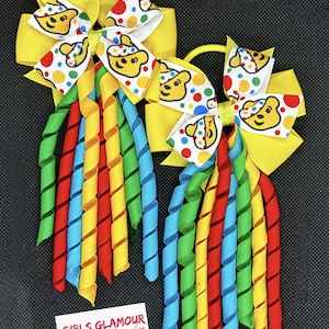 May include: Two yellow hair bows with white and colorful polka dots and a cartoon bear design. Each bow has a set of colorful curly ribbons attached.