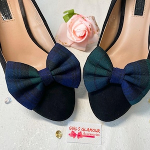 Op de afbeelding: Zwarte pumps met strikjes van blauw en groen geruit stof. Op een witte ondergrond, samen met een roze roos en een kaart met de tekst "GIRLS GLAMOUR Accessories".